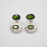 A pair of silver drop earrings with oval green gemstones, displayed on a clean white background.