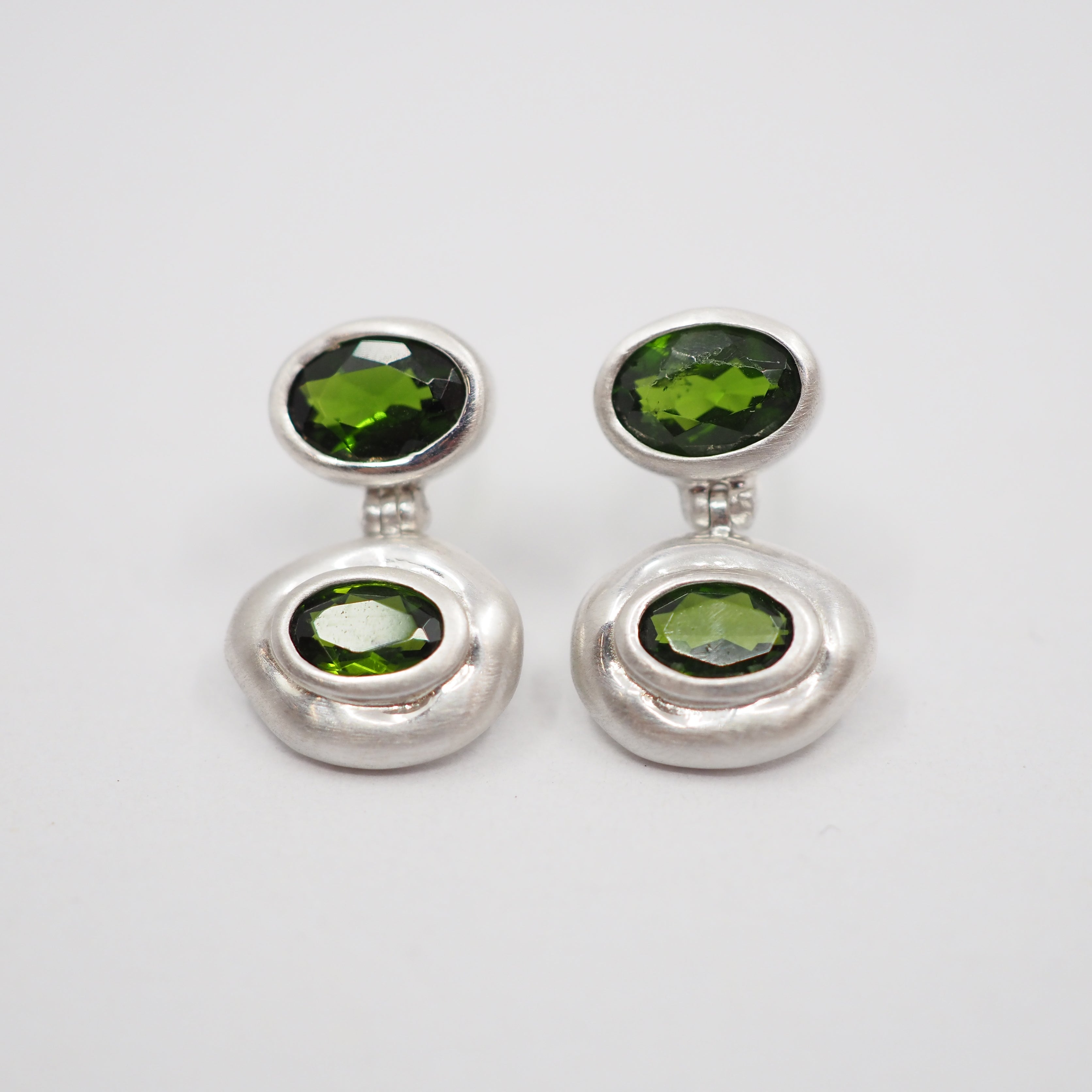 A pair of silver drop earrings with oval green gemstones, displayed on a clean white background.