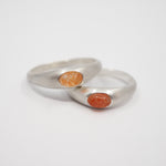 Two silver rings with oval orange cabochon gemstones, displayed on a clean white background.