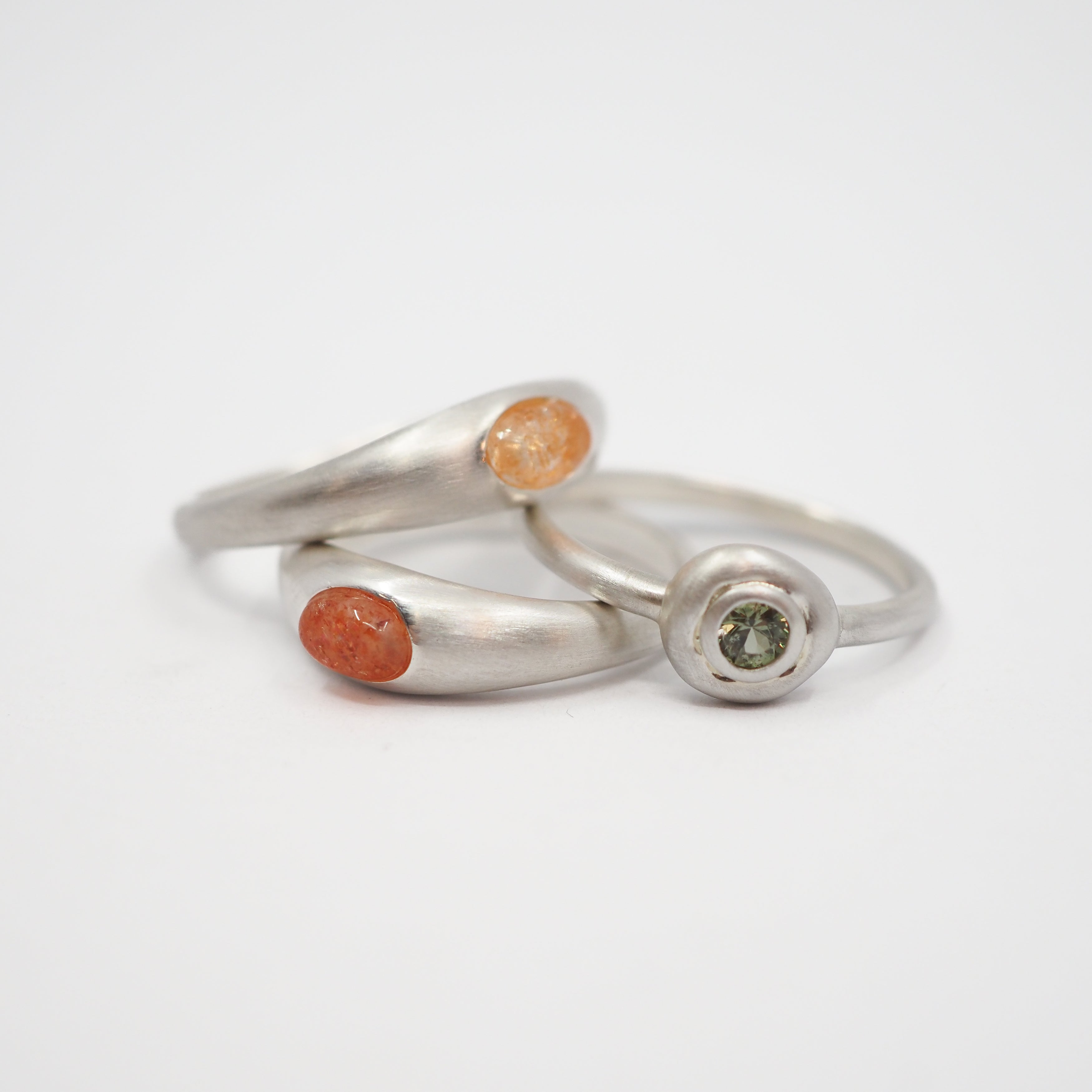 Three minimalist sterling silver rings with small natural gemstone inlays, displayed on a clean white background.