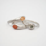 Three minimalist sterling silver rings with small natural gemstone inlays, displayed on a clean white background.