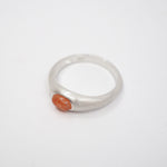 A silver ring with a small, oval-shaped orange stone set on a plain white background.