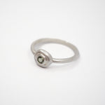 A minimalist sterling silver ring featuring a small, bezel-set round green gemstone on a clean white background.