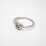 A minimalist sterling silver ring featuring a small, bezel-set round green gemstone on a clean white background.