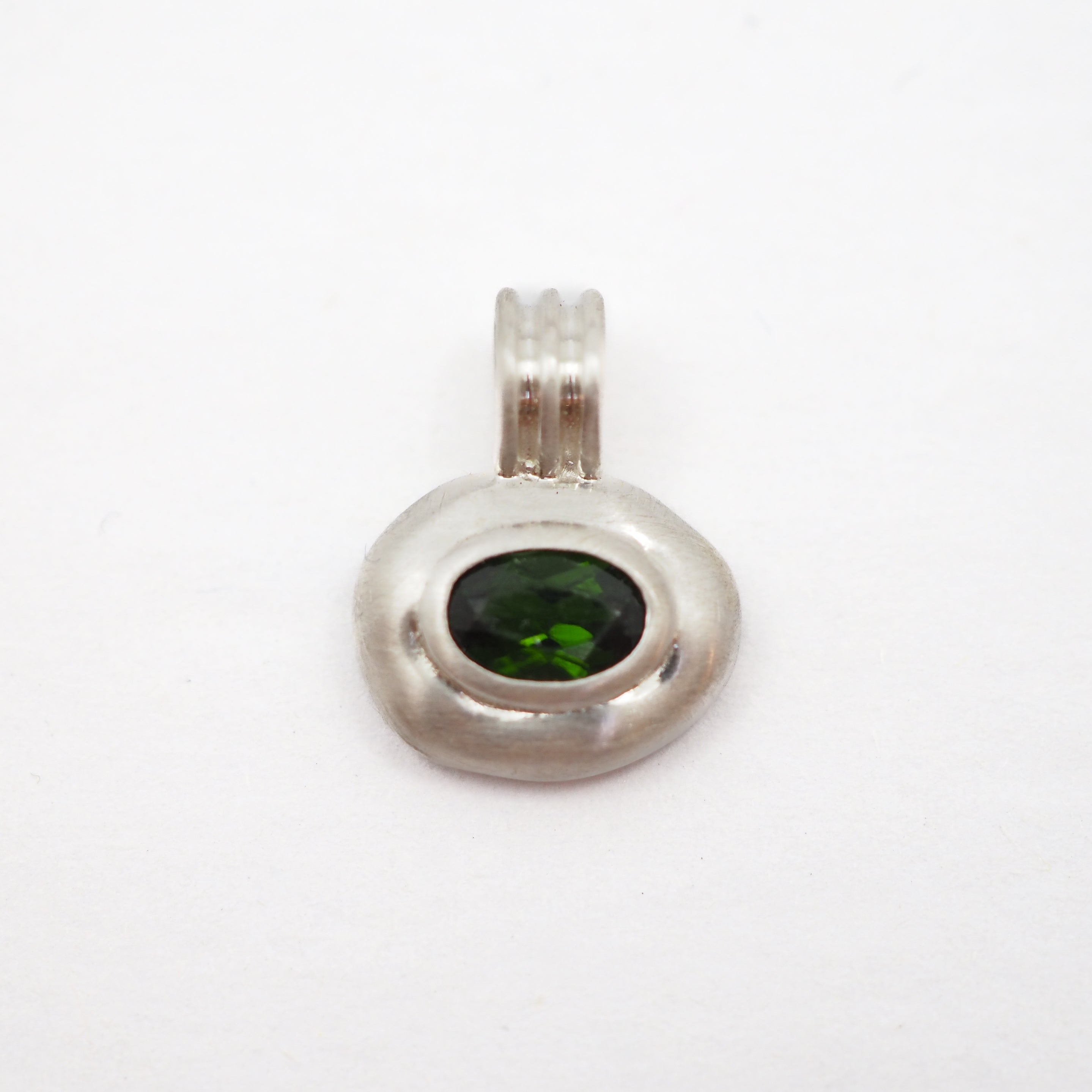 A silver pendant with a textured, organic oval shape featuring a dark green oval gemstone in the center, set against a plain white background.