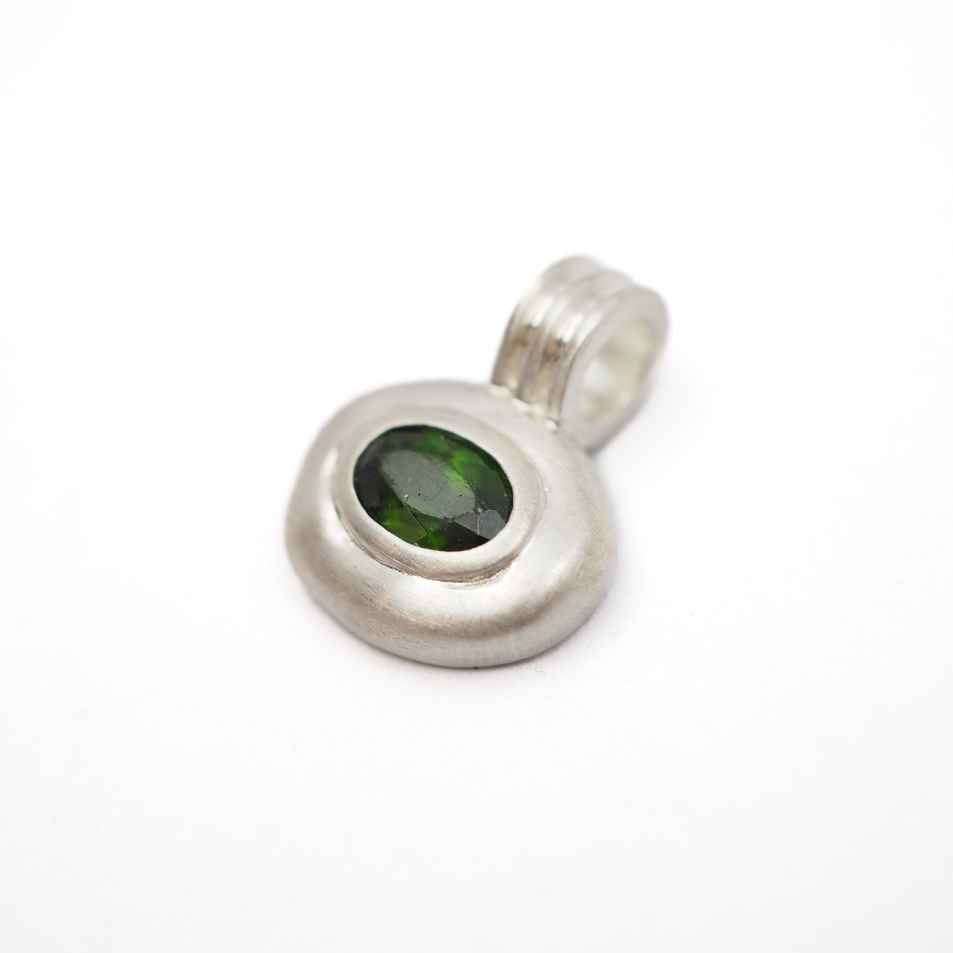 A sterling silver pendant with a textured, organic-shaped bezel setting holding a dark green oval gemstone, shown on a plain white background.