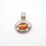 A silver pendant featuring an oval-shaped amber glass cabochon with fine gold leaf flecks, set in a textured silver bezel with a matching silver bail, shown on a plain white background.