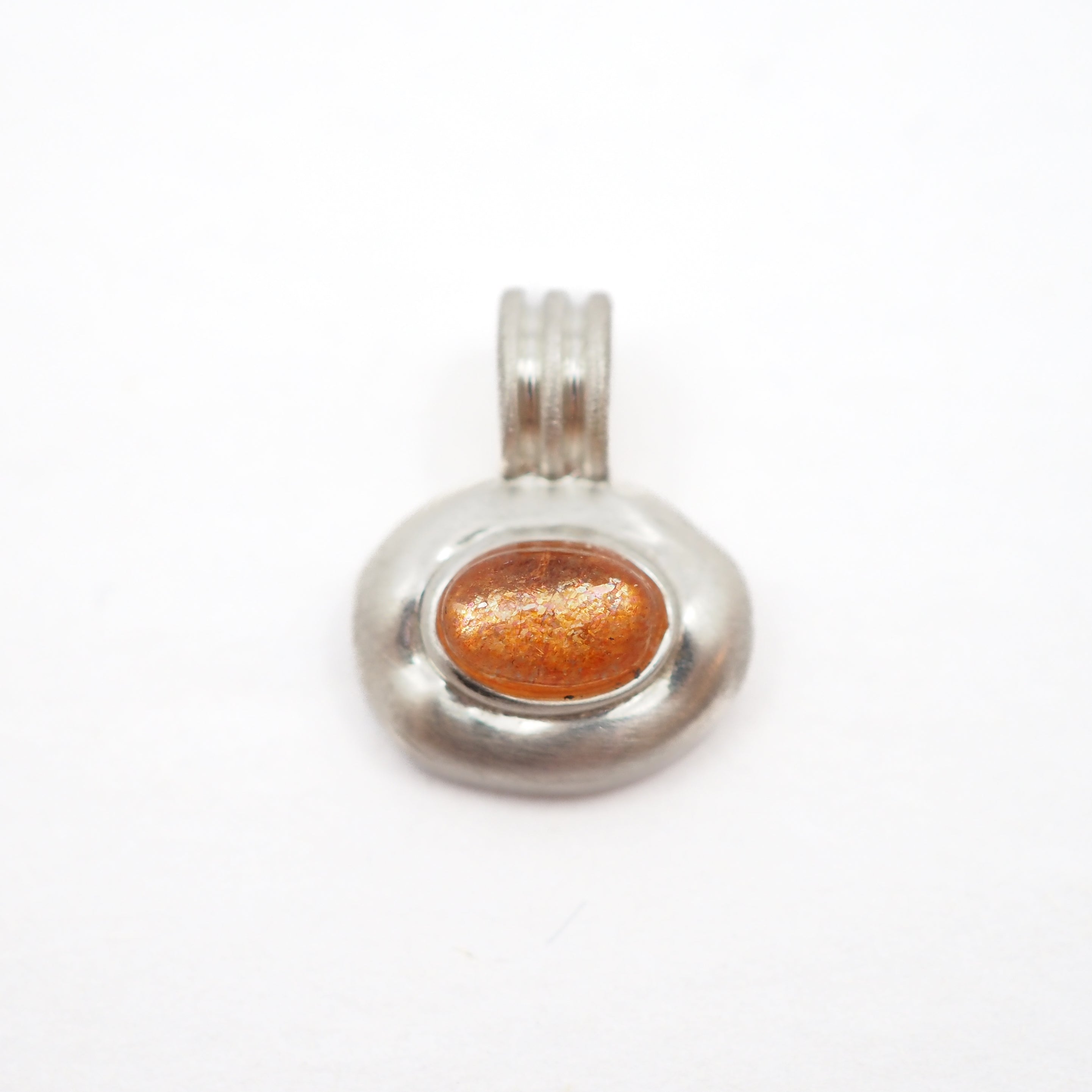 A silver pendant featuring an oval-shaped amber glass cabochon with fine gold leaf flecks, set in a textured silver bezel with a matching silver bail, shown on a plain white background.