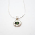 A silver pendant necklace featuring a textured, organic-shaped silver bezel holding a round green gemstone, suspended from a fine silver chain against a plain white background.