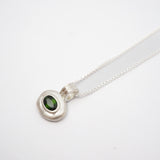 A sterling silver pendant necklace featuring a polished, organic-shaped silver bezel holding a round green gemstone, suspended from a delicate silver chain on a white background.
