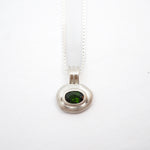 A silver pendant necklace featuring a bezel-set oval green gemstone on a delicate silver chain, photographed against a plain white background.