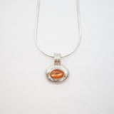 A silver pendant necklace featuring a textured silver bezel holding a small, oval-shaped orange gemstone, suspended from a delicate silver chain against a plain white background.