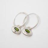 A pair of silver hoop earrings with small, irregular silver pendants set with oval green gemstones, shown on a plain white background.