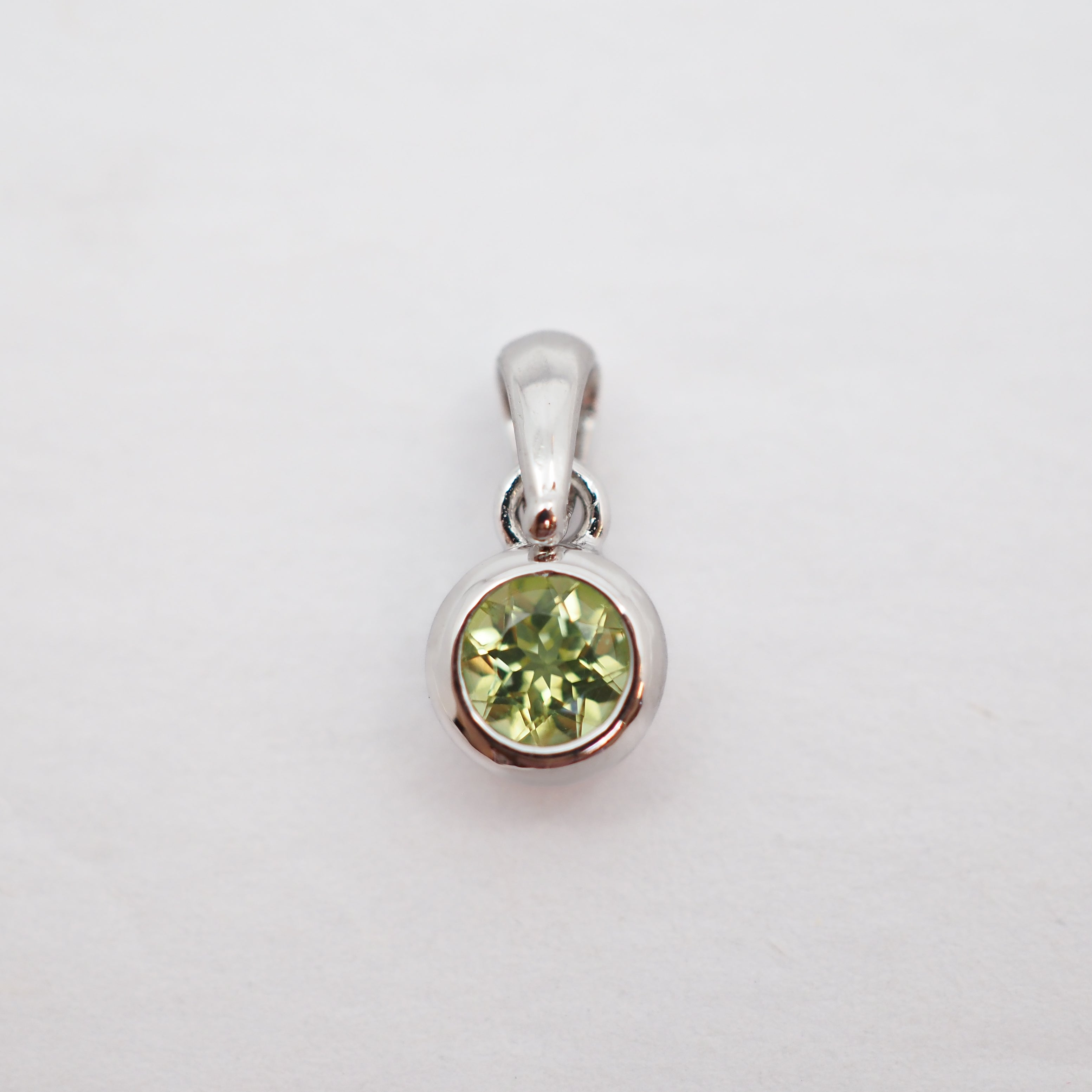 A sterling silver pendant featuring a round-cut light green gemstone in a bezel setting, shown on a plain white background.