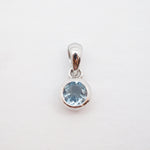 A sterling silver pendant featuring a round-cut light blue gemstone in a bezel setting, suspended from a polished bail against a plain white background.