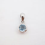 A sterling silver pendant featuring a round-cut light blue gemstone in a bezel setting, suspended from a polished bail against a plain white background.