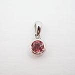 A silver pendant with a round pink gemstone in a bezel setting, shown on a plain white background.