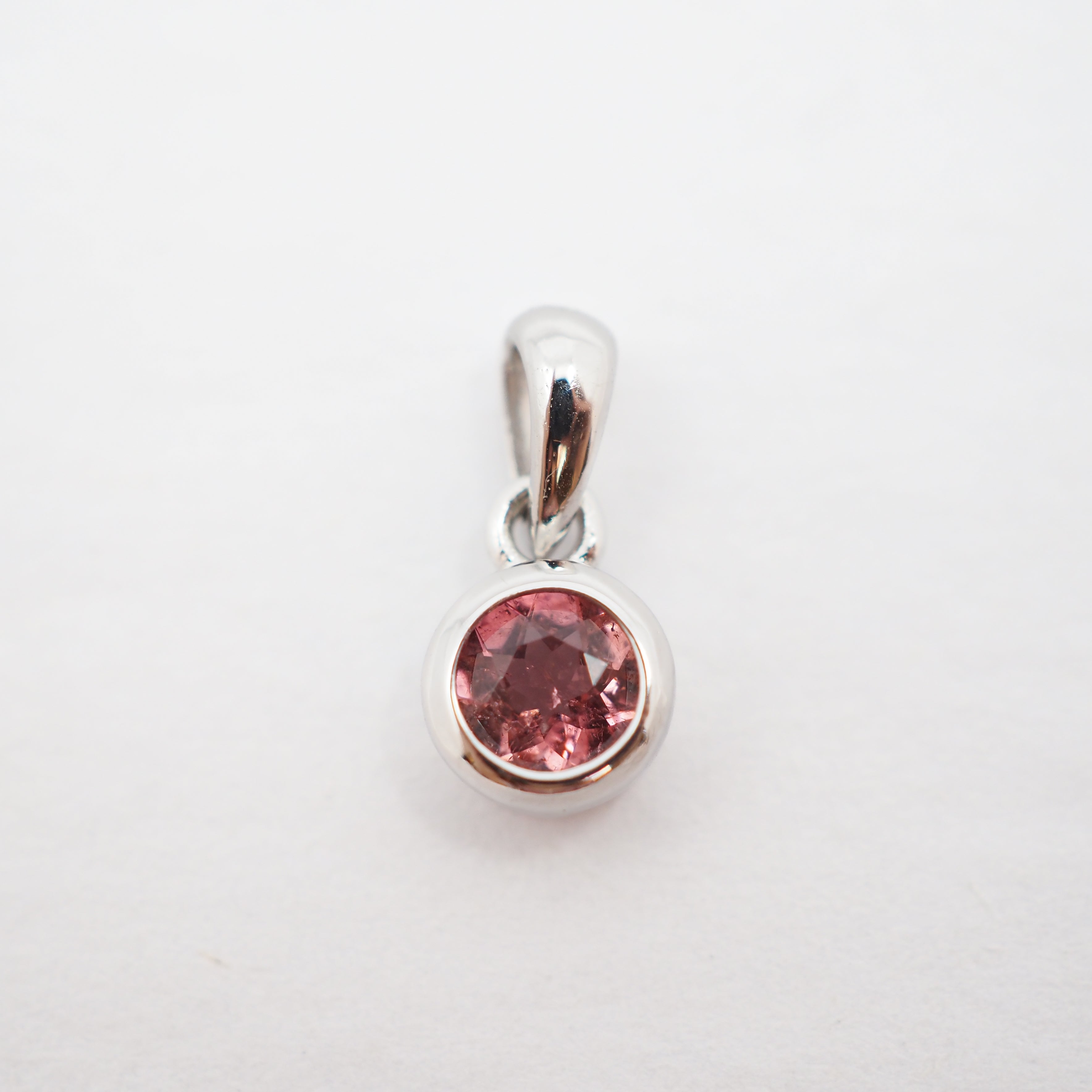 A silver pendant with a round pink gemstone in a bezel setting, shown on a plain white background.