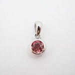 A silver pendant with a round pink gemstone in a bezel setting, shown on a plain white background.