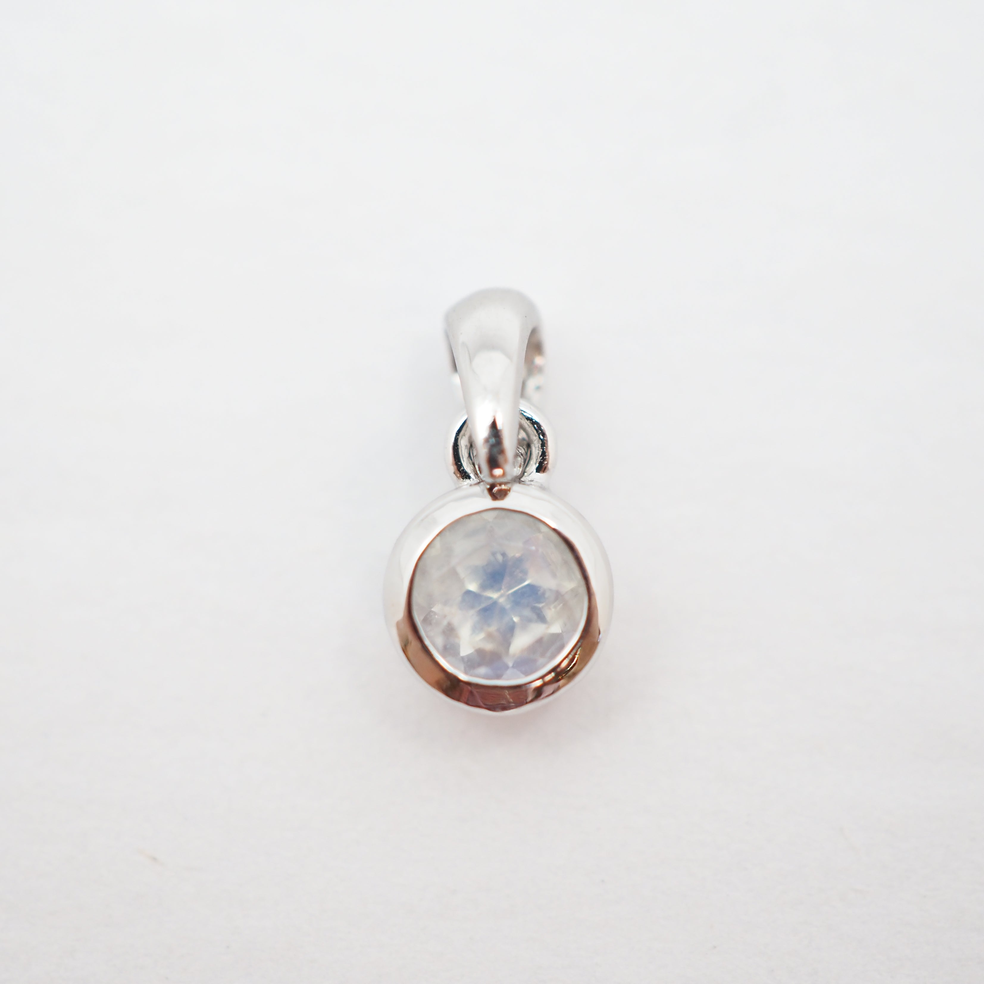A sterling silver pendant charm featuring a bezel-set round iridescent moonstone gemstone, shown on a plain white background.