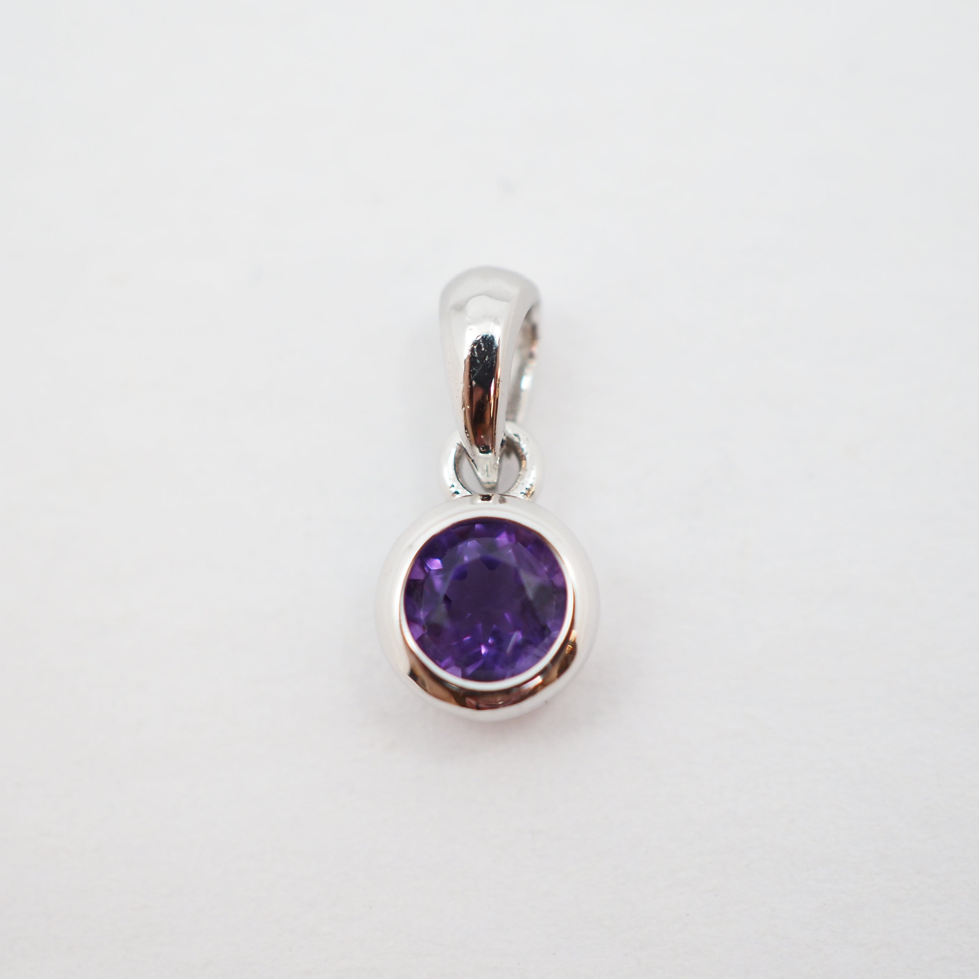 A sterling silver pendant charm featuring a round-cut purple gemstone in a bezel setting, shown on a plain white background.