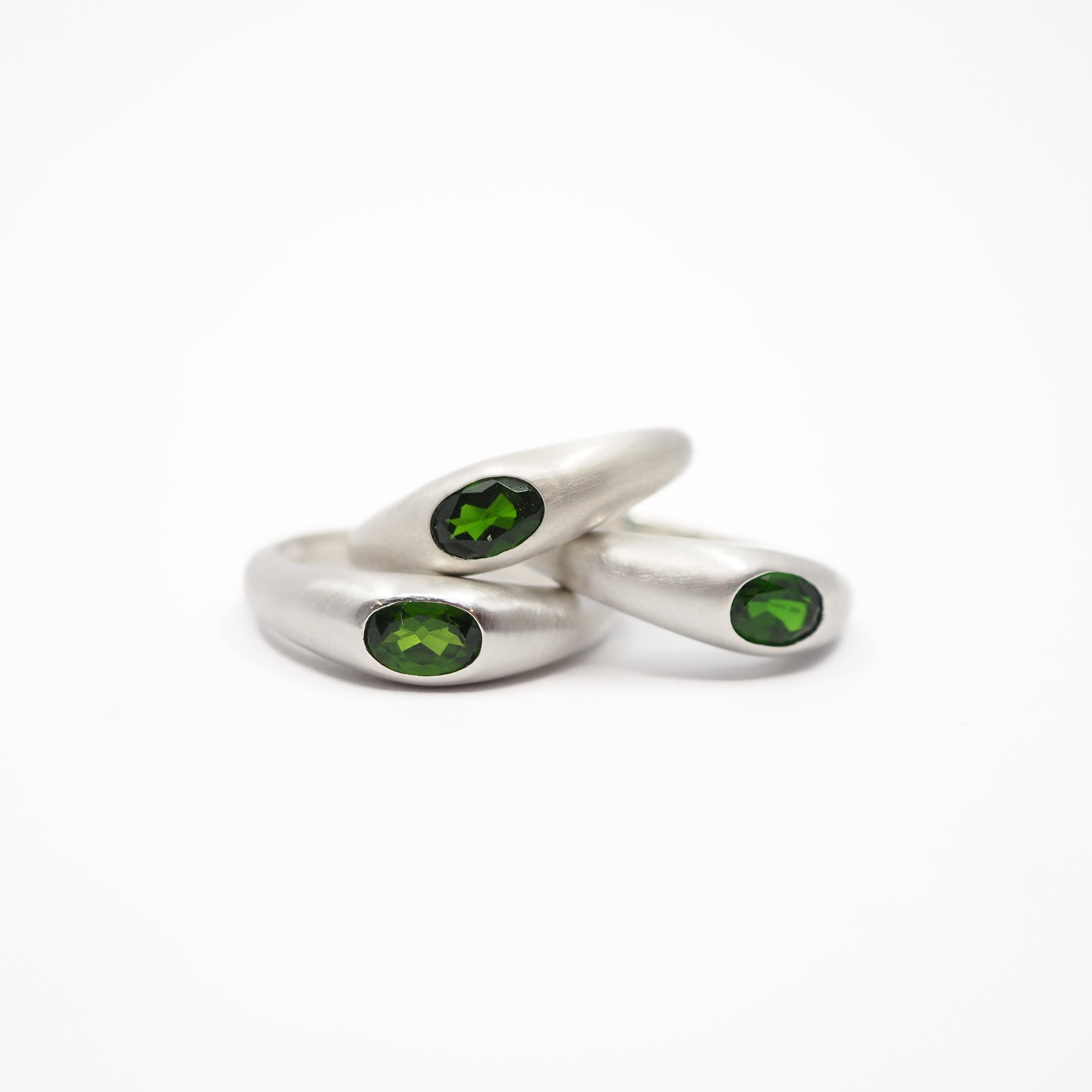 three silver curved rings with oval green gemstones, photographed on a clean white background.