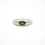 A silver band ring featuring a round green gemstone in a bezel setting, photographed against a seamless white background.