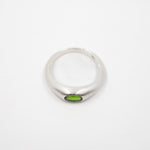 A silver band ring featuring a small oval green gemstone set in the center, photographed on a plain white background.