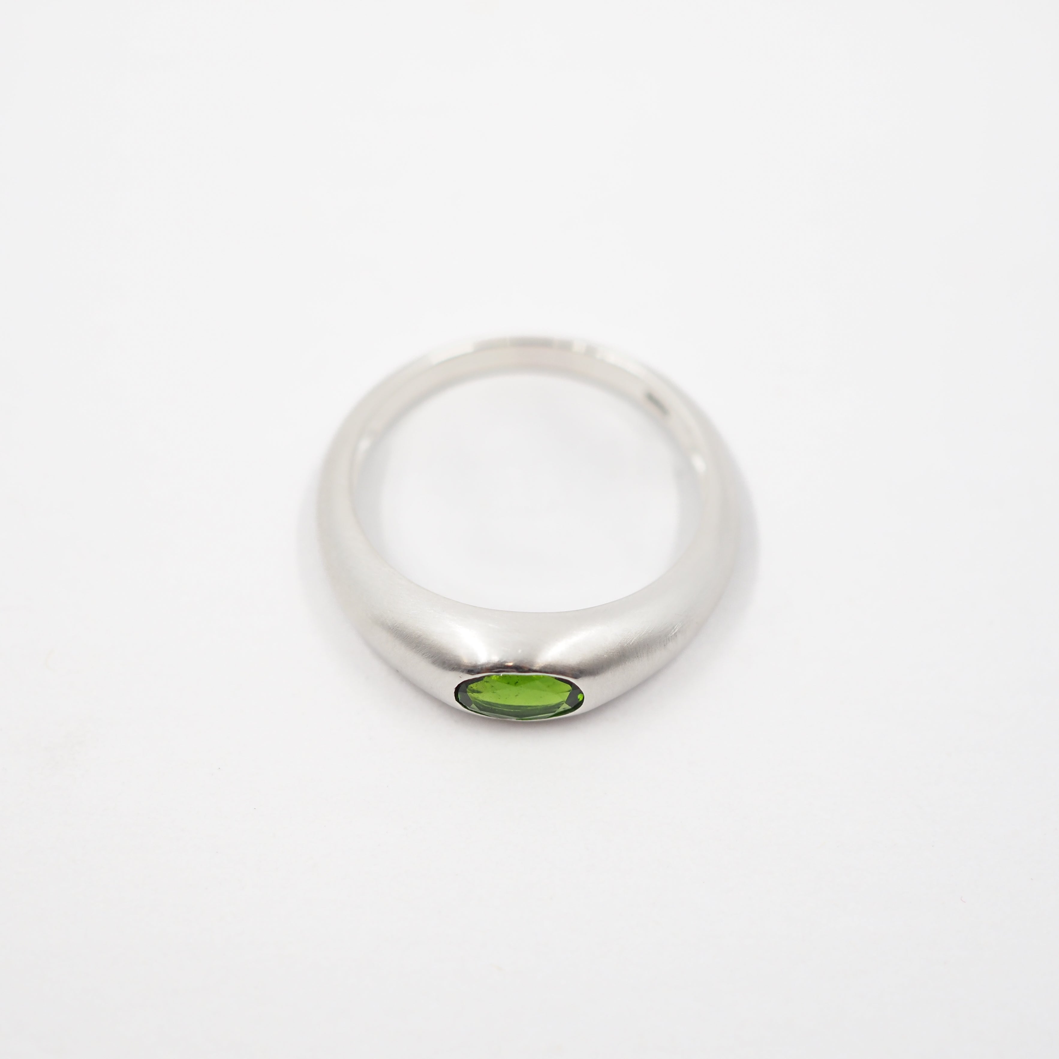 A silver band ring featuring a small oval green gemstone set in the center, photographed on a plain white background.