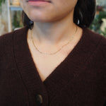 A close-up of a person wearing a delicate gold chain necklace styled with a dark brown knit cardigan.