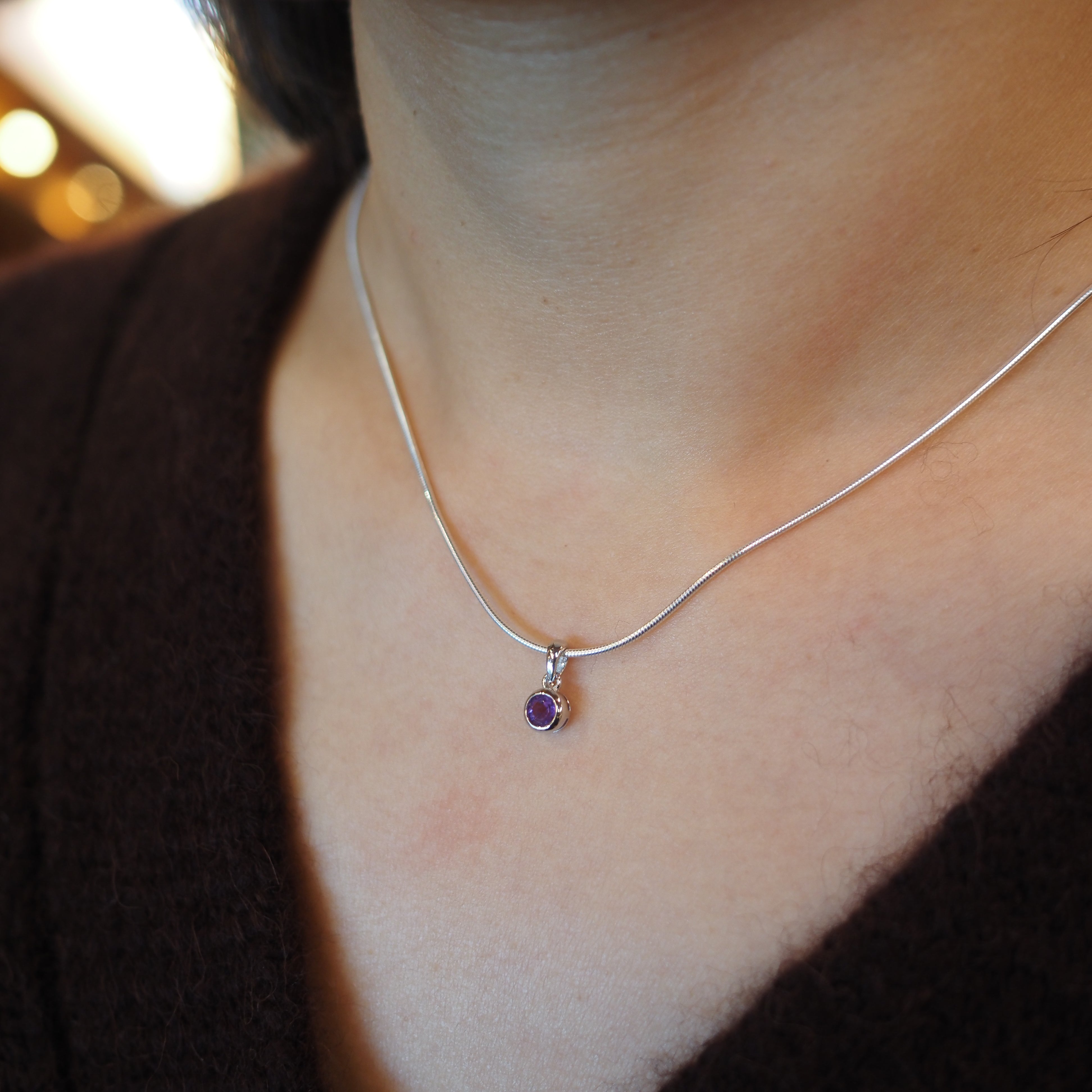A close-up of a person's neck and chest wearing a delicate silver chain necklace with a small purple pendant.