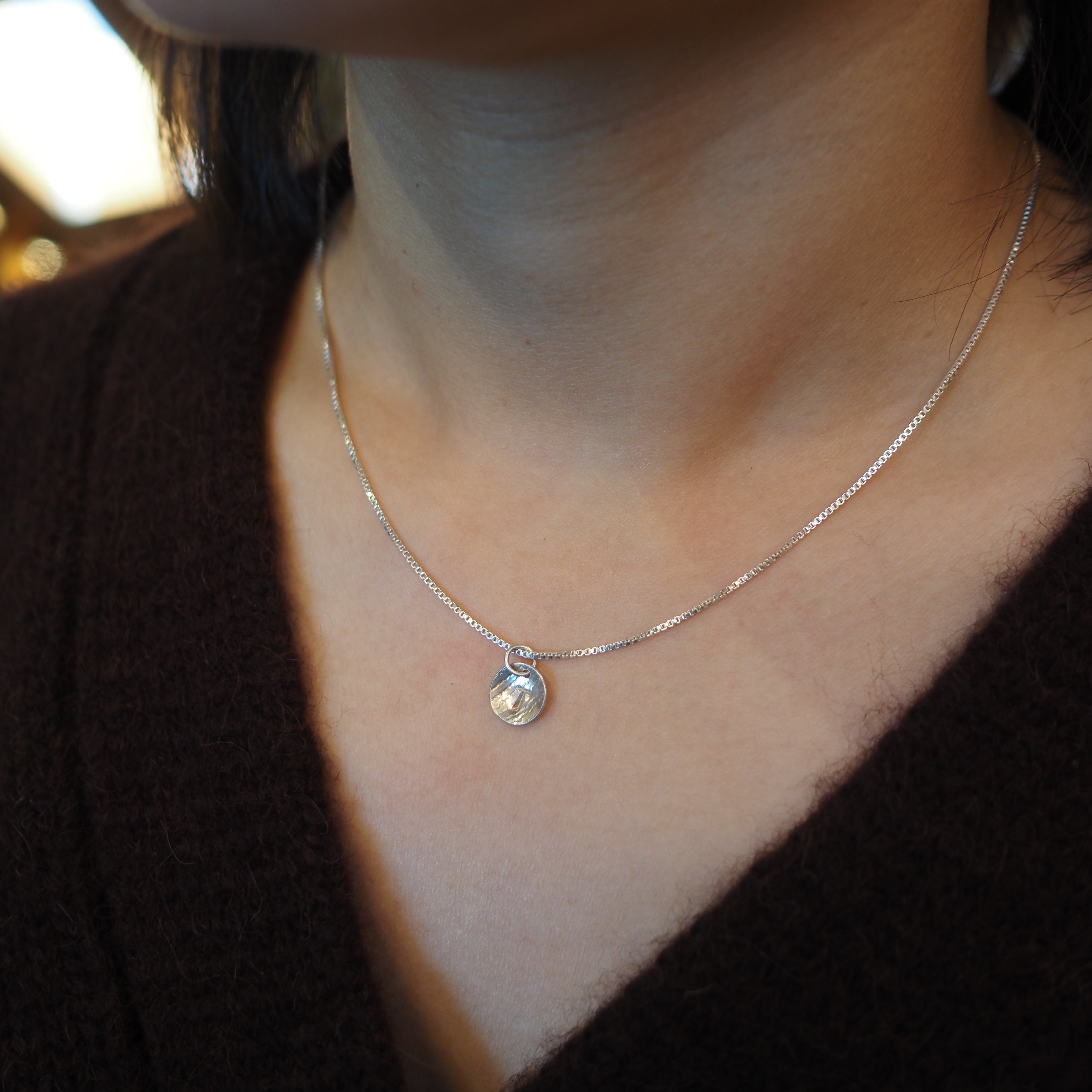 A close-up of a person's neck and chest wearing a delicate silver chain necklace with a small, faceted clear teardrop pendant.