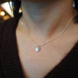 A close-up of a person's neck and chest wearing a delicate silver chain necklace with a small circular silver pendant.