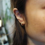 A close-up of a person's ear wearing a small, polished gold hoop earring.