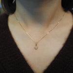 A delicate gold chain necklace with a small round pendant, shown worn on a person's neck over a dark brown knit top.