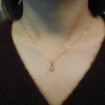 A delicate gold chain necklace with a small round pendant, shown worn on a person's neck over a dark brown knit top.