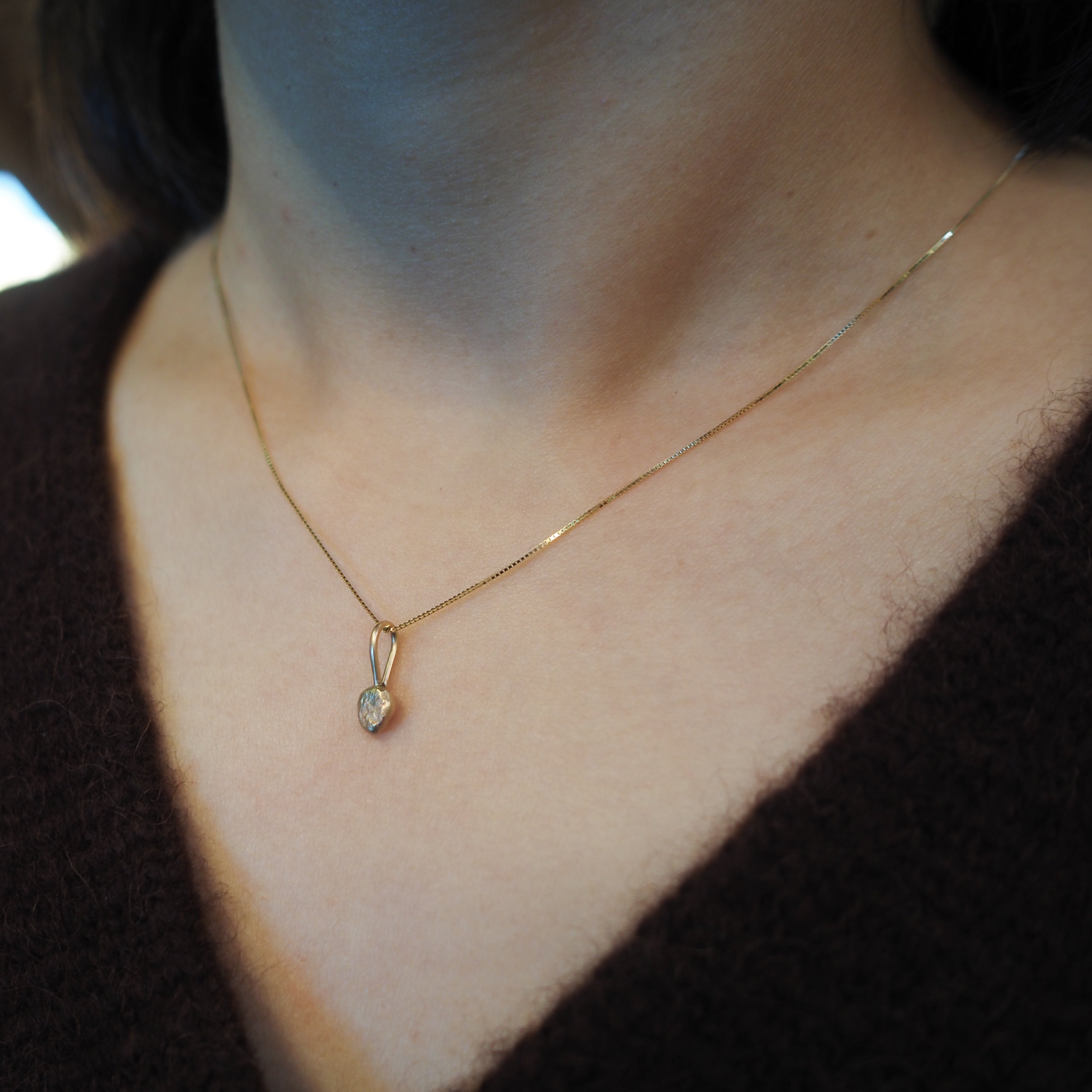 A close-up of a person's neck and chest wearing a delicate gold chain necklace with a small teardrop-shaped pendant.