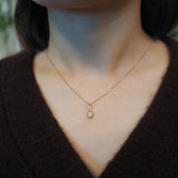 A close-up of a person's neck and chest wearing a delicate gold chain necklace with a small pendant, paired with a dark brown knit V-neck sweater.