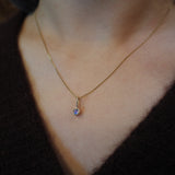A close-up of a person's neck and chest wearing a delicate gold chain necklace with a small bezel-set oval purple gemstone pendant.