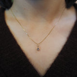 A close-up of a person's neck and chest wearing a delicate gold chain necklace with a small teardrop-shaped clear gemstone pendant.