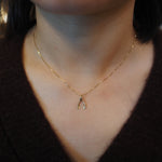 A close-up of a person's neck and chest wearing a delicate gold chain necklace with a small wishbone pendant.