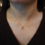 A close-up of a person's neck and chest wearing a delicate gold chain necklace with a small wishbone pendant.