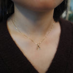 A close-up of a person's neck and chest wearing a delicate gold chain necklace with a small gold wishbone pendant.