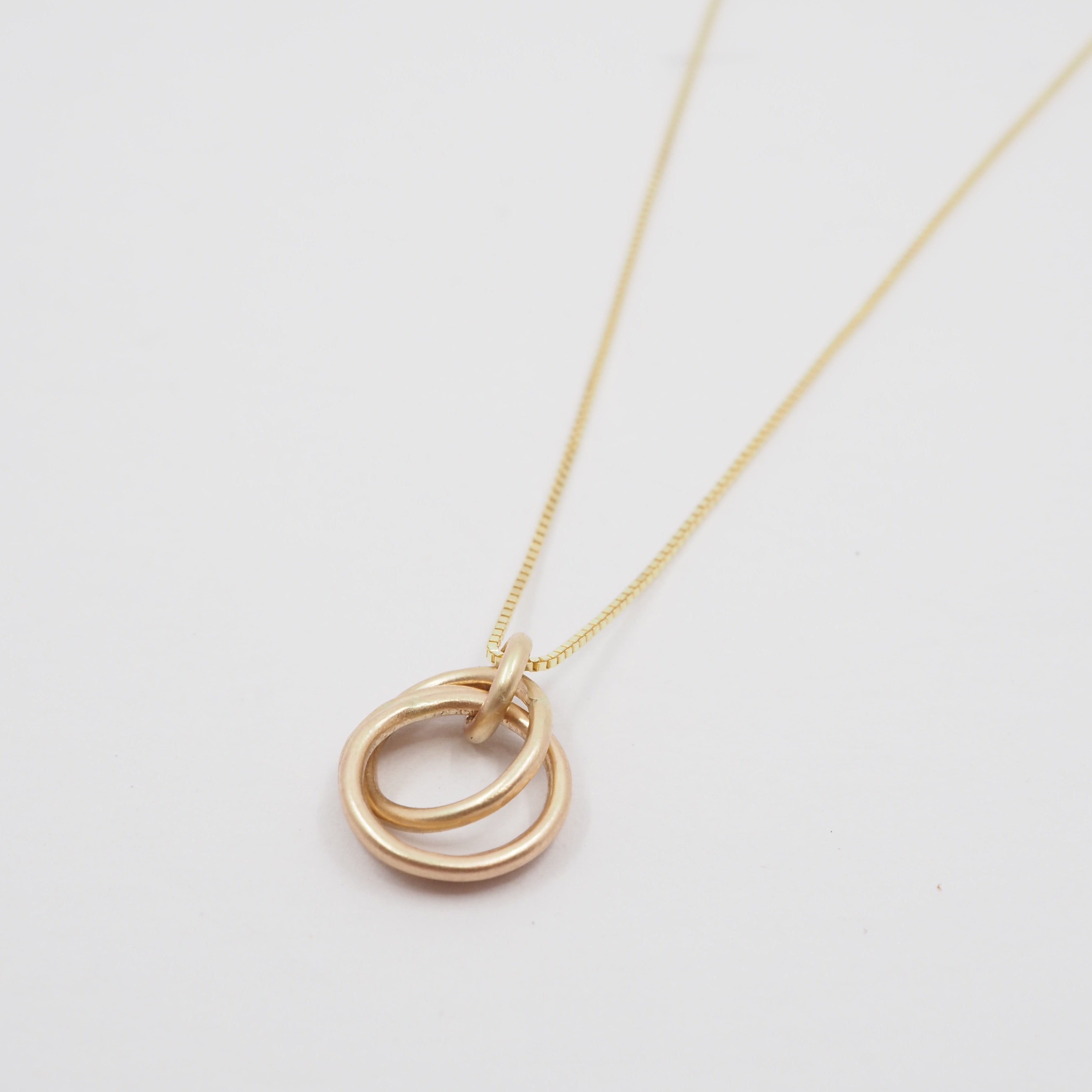 Gold necklace with a double ring pendant on a light gray background