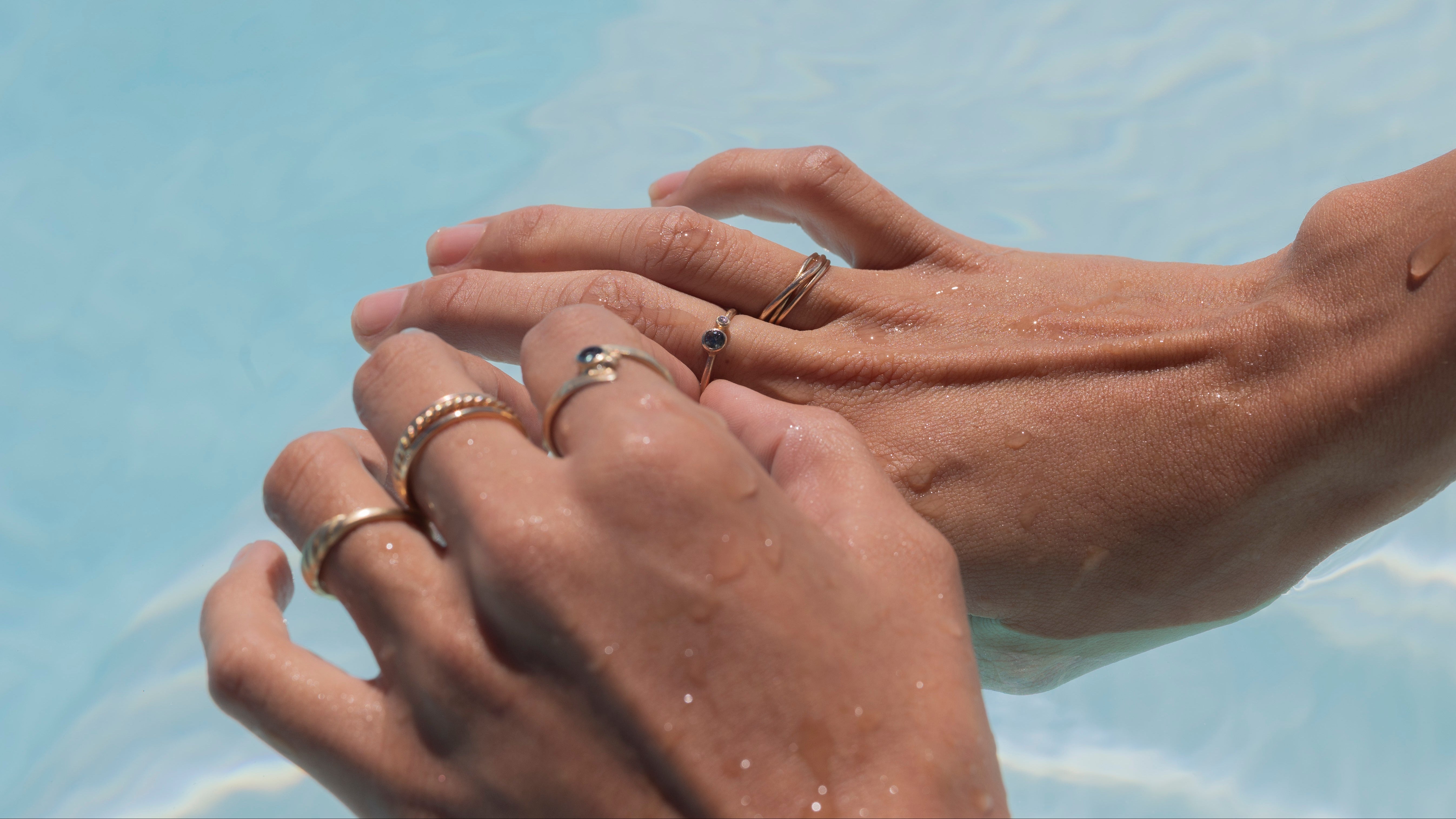 Close-up of two hands with rings on a clear blue, pool water background