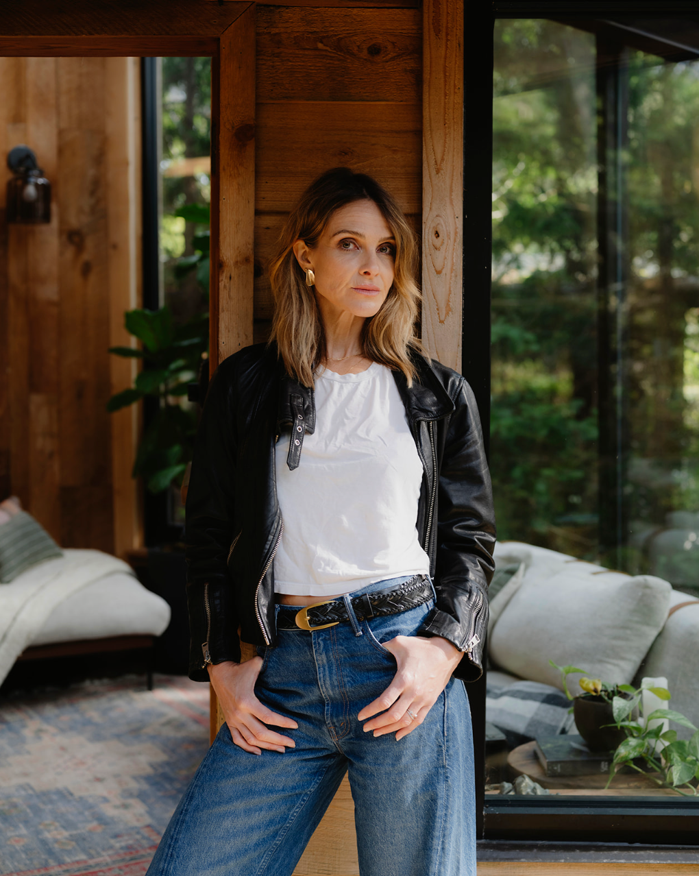 Woman standing with gold earrings, a black leather jacket and jeans