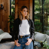 Woman standing with gold earrings, a black leather jacket and jeans