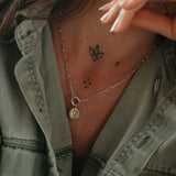 Person wearing a necklace with a pendant, showing tattoos on neck and shoulder.