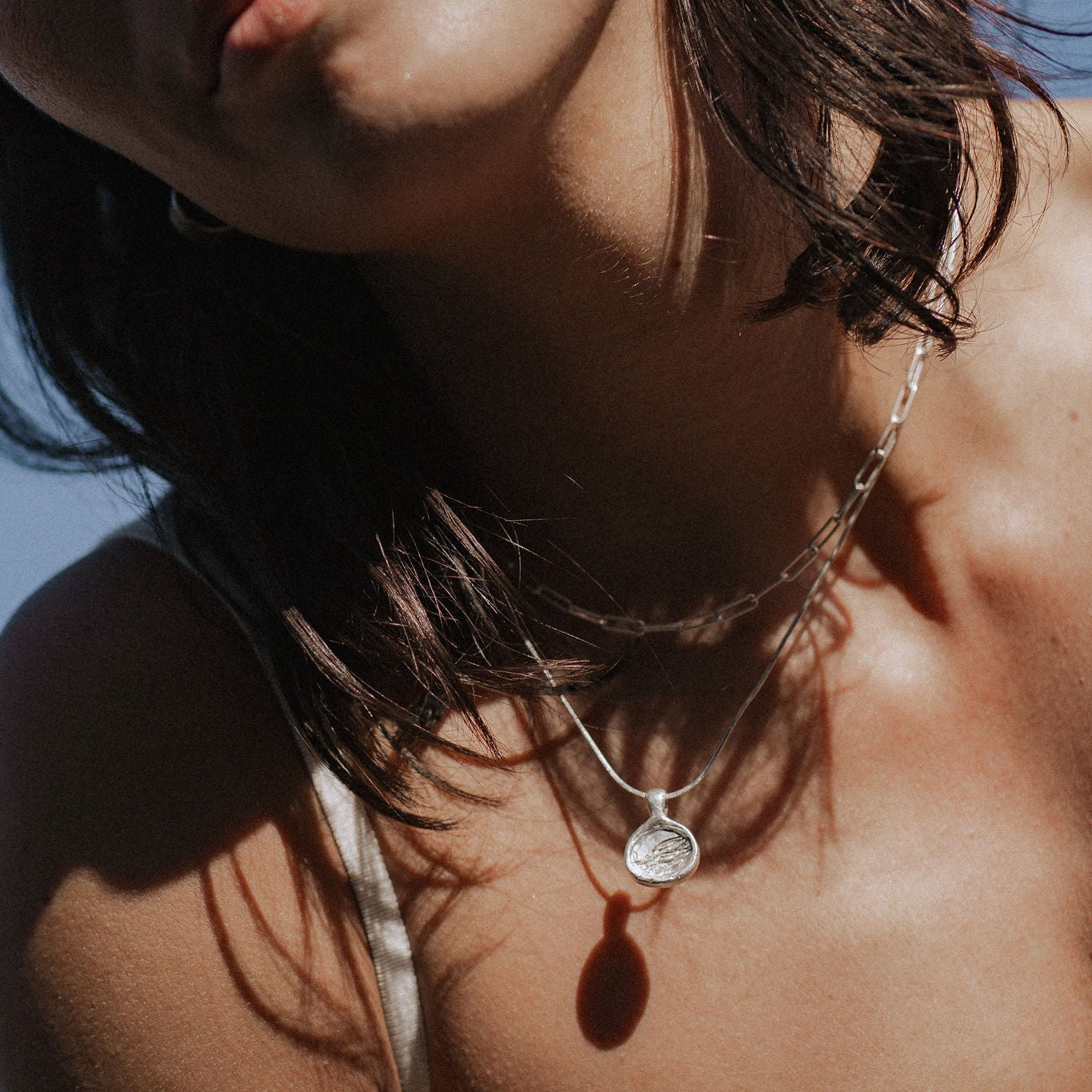 Close-up of a person wearing a necklace with a pendant against a blue sky.